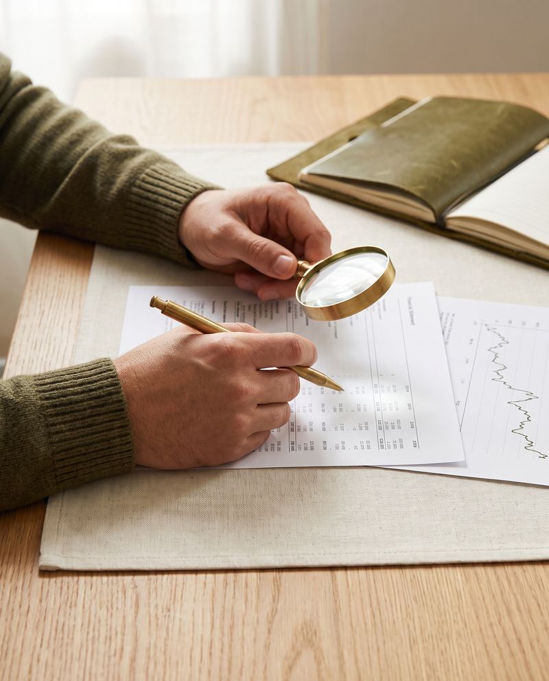 Mãos conferindo com lupa uma demonstração financeira impressa